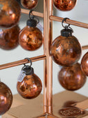Close-up of copper-toned decorative hanging ornaments with a distressed metallic finish, displayed on a copper-colored stand.