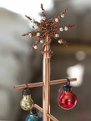 A copper Christmas tree topper with a wire star ornament and hanging vintage-style Christmas bulbs in red, gold, and blue, shown against a blurred neutral background.