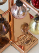 Close-up of a copper-colored metal decorative stand with hanging glass ornaments and a circular base embossed with the words 'deus living'.