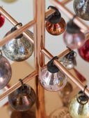 Close-up of a copper geometric tree ornament holder with hanging metallic Christmas baubles in silver, gold, pink, and red.