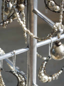 Close-up of silver-toned beaded jewelry hanging from a metal display stand, including crescent moon and pearl-style ornaments.