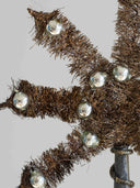 A close-up of a brown tinsel star decoration adorned with clear glass ornaments, set against a plain light gray background.