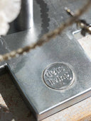 Close-up of a silver-toned metal jewelry-making tool with a circular recessed logo stamped with the words 'deus living' and a chain partially visible in the foreground.